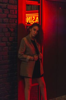 Stylish woman wearing blazer posing in vibrant red neon light at night.