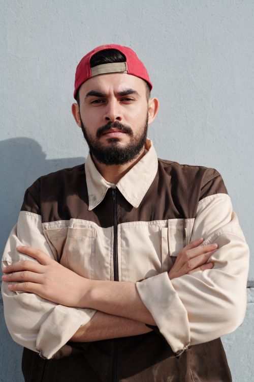 Free Portrait of a bearded man in a cap posing confidently outdoors with arms crossed. Stock Photo