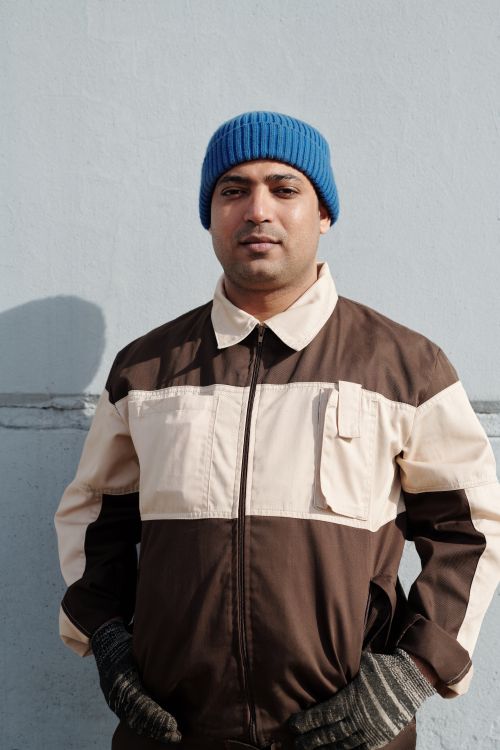 Free Man wearing a blue beanie and gloves, standing against a wall, portraying a focused expression. Stock Photo