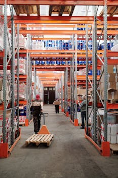 Workers arrange inventory on shelves in a large industrial warehouse.