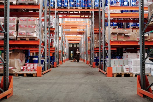 A spacious industrial warehouse with stocked shelves and a worker in protective gear.
