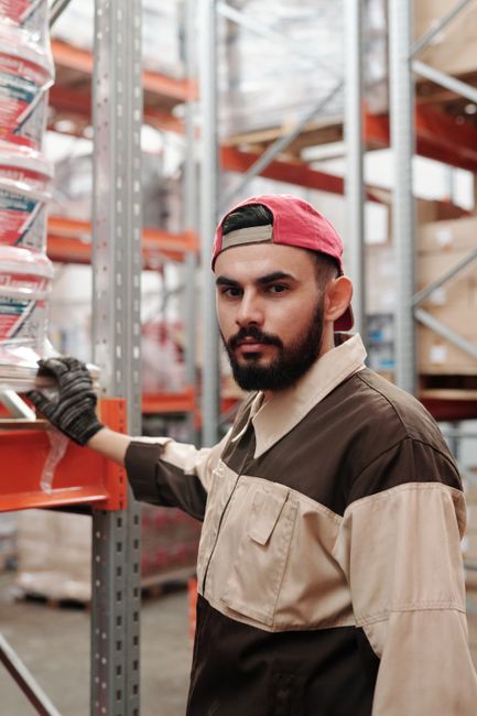 Portrait of a bearded man in a warehouse wearing a red cap and work uniform. Portrait of a bearded man in a warehouse wearing a red cap and work uniform.