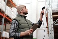 在室内，男性仓库工作人员使用手持扫描仪和平板电脑扫描库存
