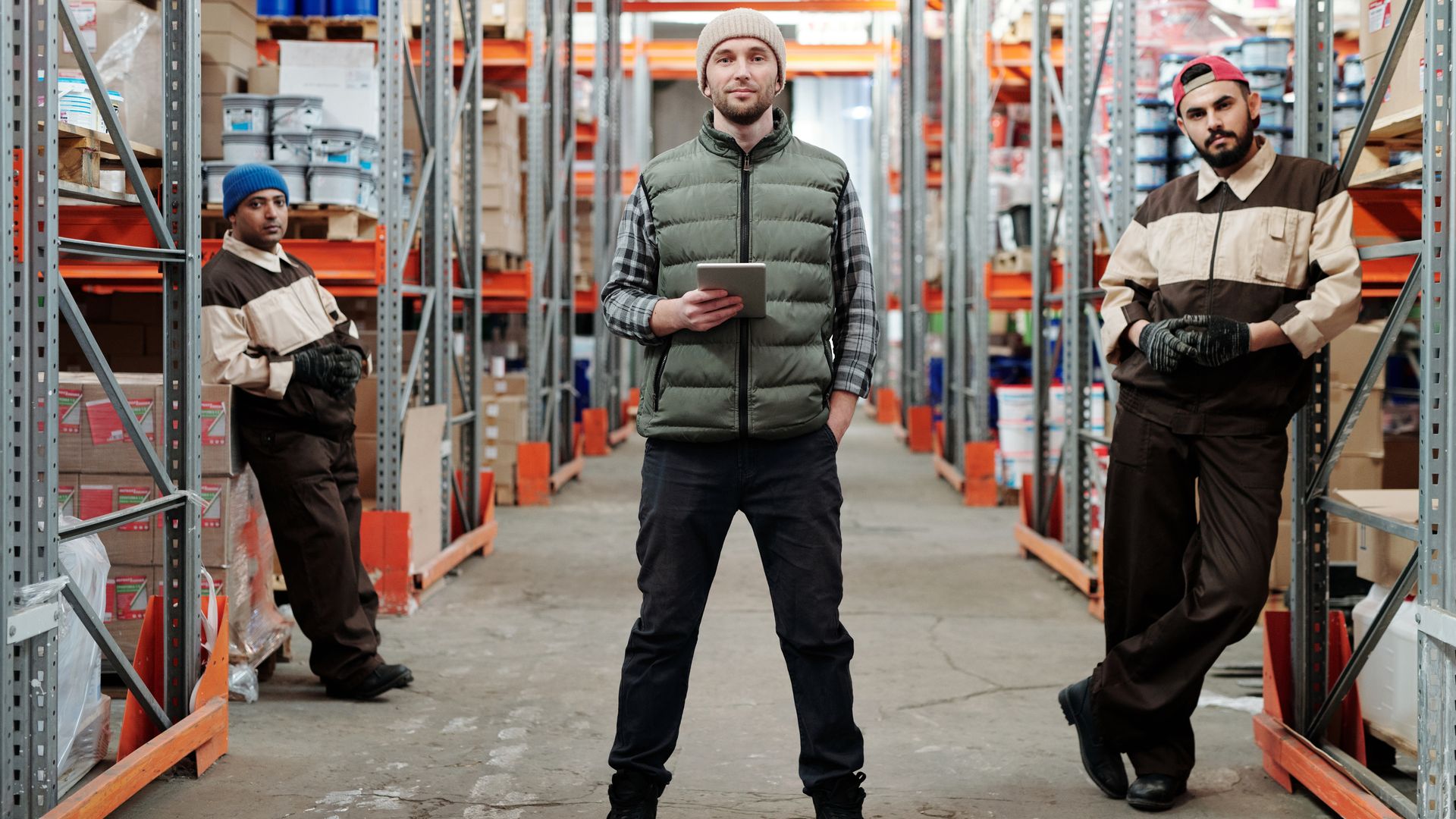 Three men in a warehouse standing among shelves with inventory — logistics business category classification