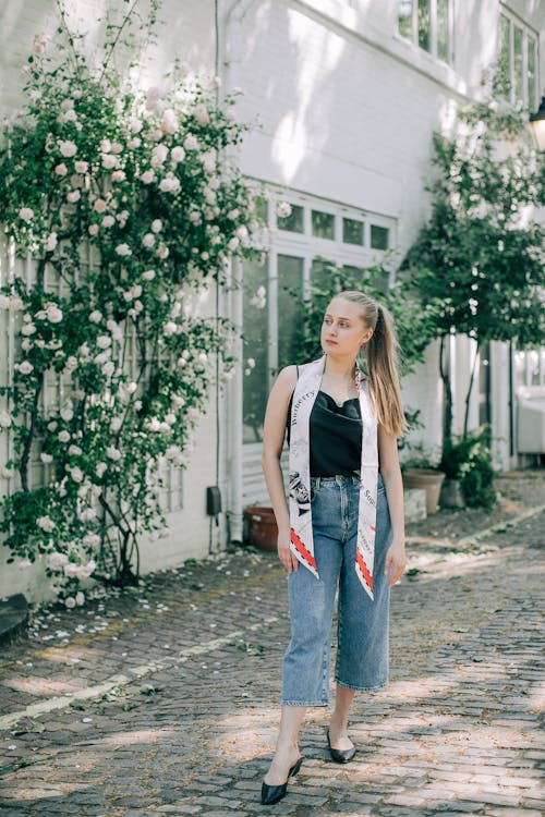 Wanita Dengan Tank Top Hitam Dan Jeans Denim Biru Berdiri Di Atas Jalan