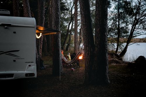 Free Cozy campsite with a camper van by a serene lake in Lithuania's forest. Ideal outdoor getaway. Stock Photo