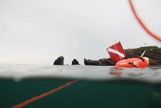 Red inflatable buoy with scuba flag floating in sea water near rocky formations
