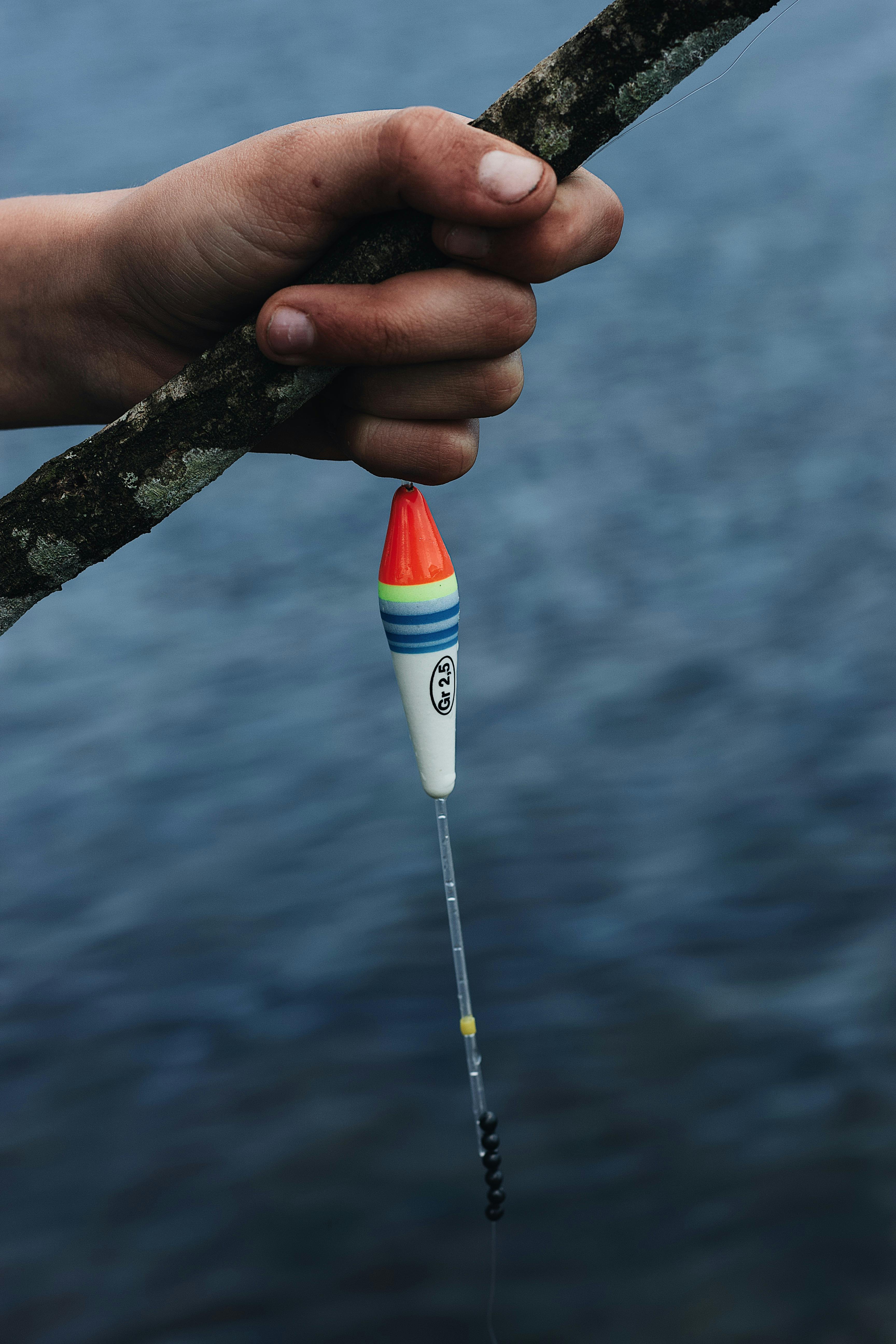 Close-up of a hand holding a colorful fishing lure against the backdrop of a serene lake.