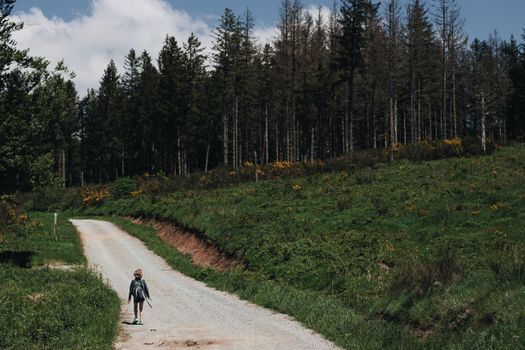 A child walks down a serene forest path on a sunny summer day, surrounded by lush greenery.
