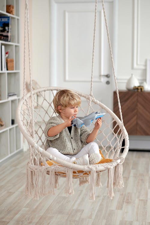 Photo of Child Sitting on Wicker Swing While Playing With Toy Plane