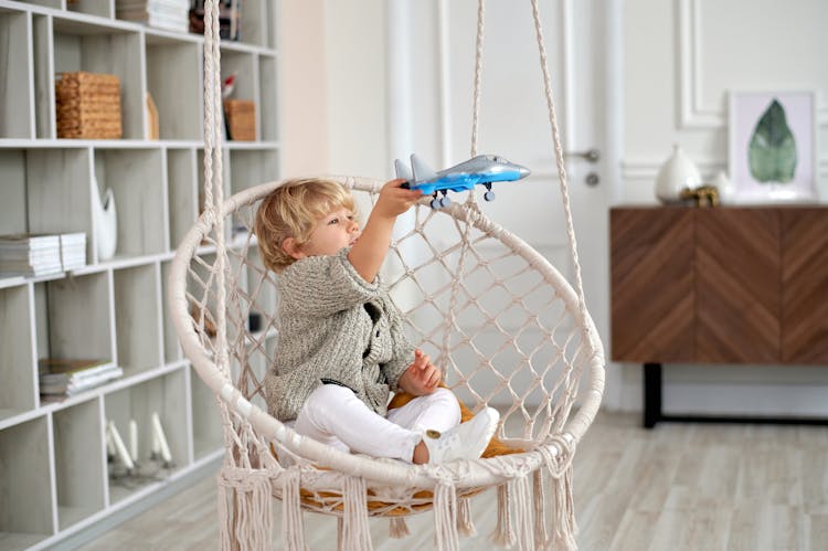 Boy Sitting On Wicker Swing While Playing With Toy Plane