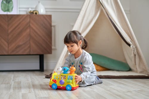 プラスチックのおもちゃの車で遊ぶ灰色のセーターの女の子