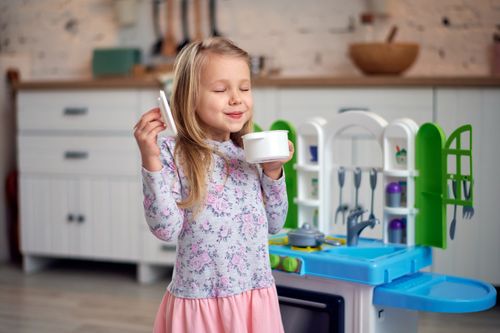 Free Happy child with blonde hair playing with a toy kitchen and enjoying a pretend tea party. Stock Photo