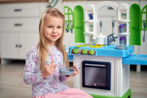 Free Cute child enjoying a playful moment with a toy kitchen set indoors, smiling happily. Stock Photo