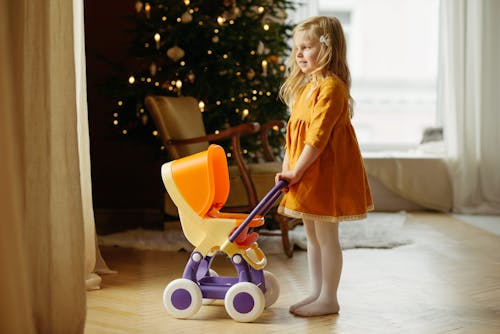 Girl in Orange Dress Standing While Holding Baby Stroller