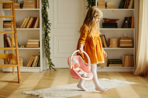 Girl in Orange Dress Walking While Carrying Baby Doll