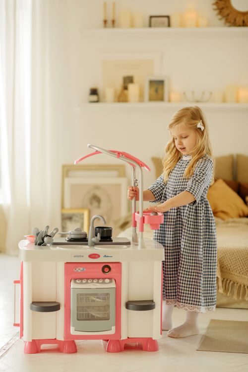 Free A young girl enjoys imaginative play with a toy kitchen in a cozy indoor setting. Stock Photo