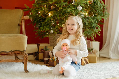 Girl in White Long Sleeve Shirt Carrying Baby Doll