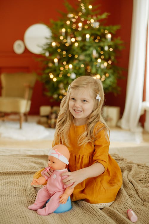 Girl in Orange Dress Smiling While Holding Baby Doll