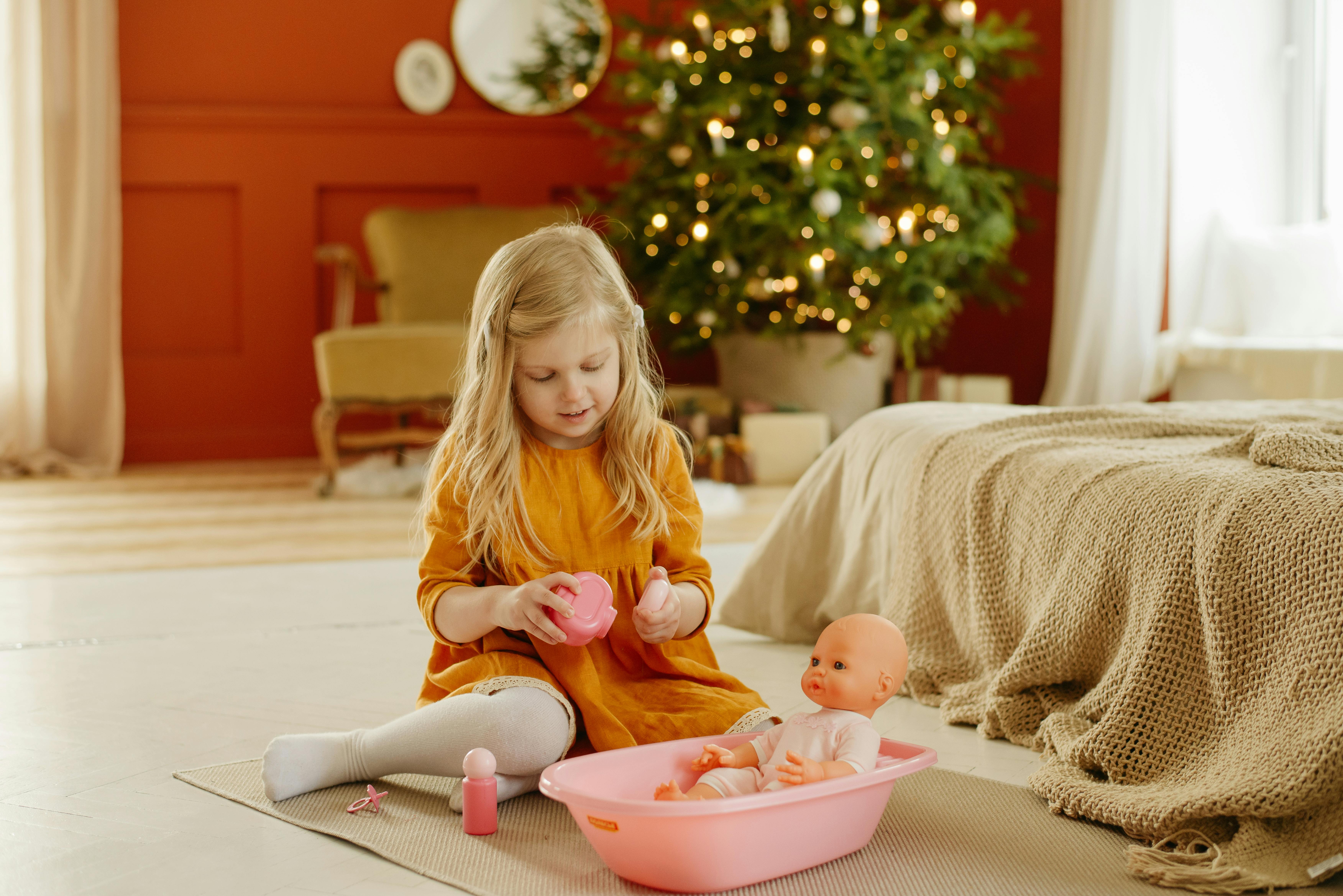 girl in orange dress playing with baby doll