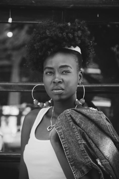 Free Black and white portrait of confident young curly haired African American female with hoop earrings and denim jacket looking at camera against blurred urban background Stock Photo