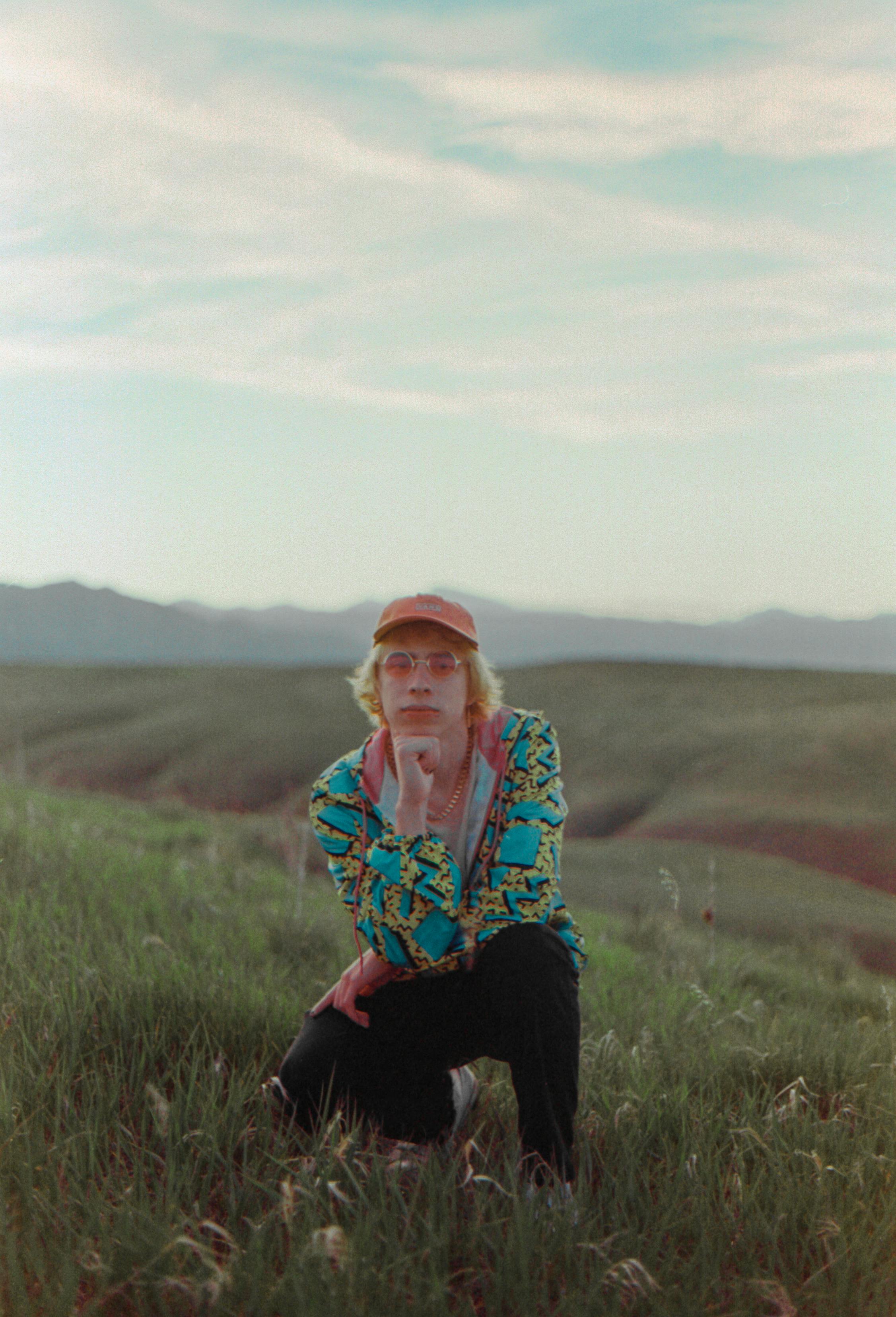 Fashionable man with sunglasses and cap posing in a serene countryside field