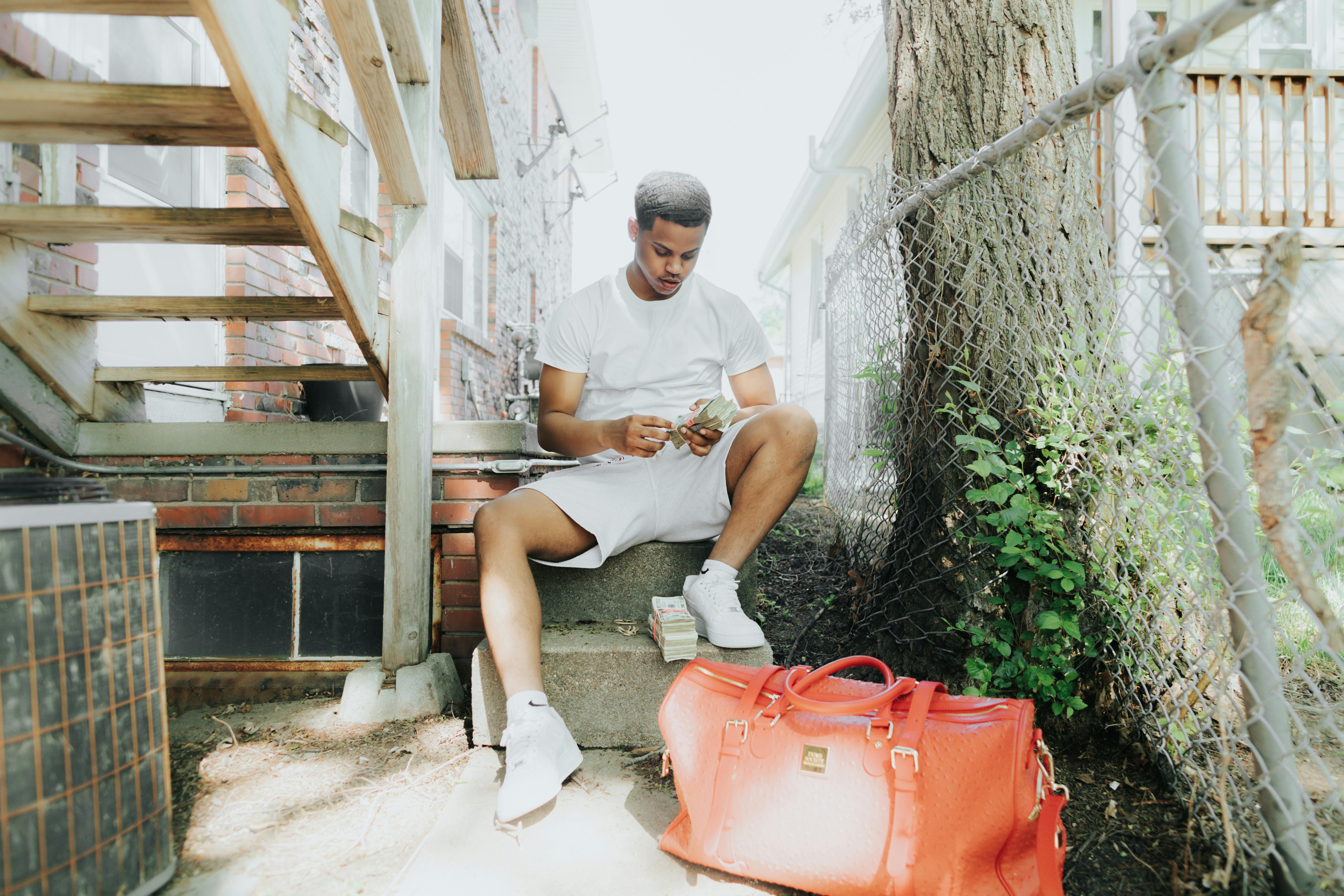 a young man counting cash while sitting near a duffle bag