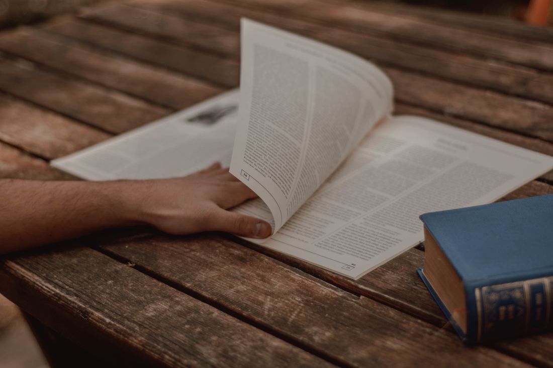 A hand resting on a wooden table beside an open book — photo by Ahmet Polat on Pexels