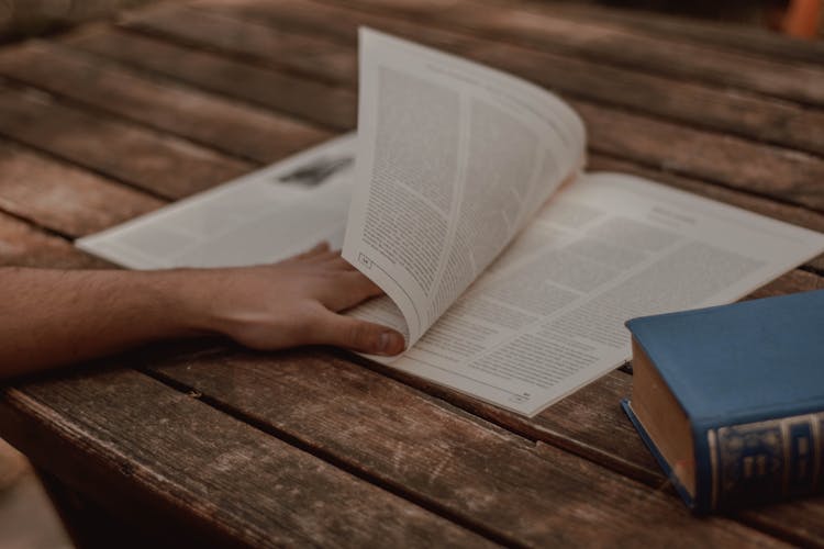 Crop Man Turning Over Page Of Magazine At Wooden Table