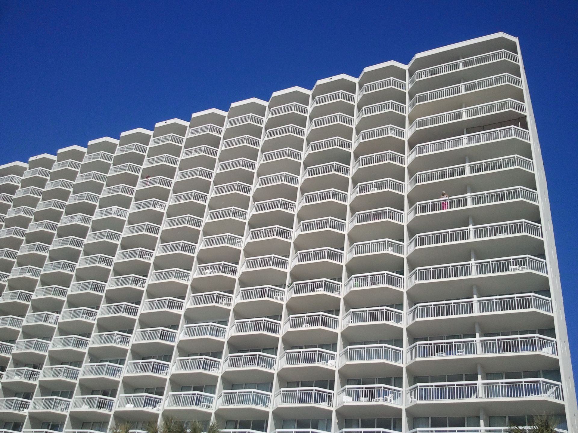 A modern high-rise apartment building with multiple balconies against a clear blue sky.