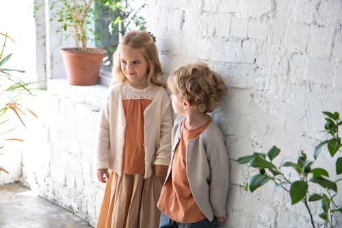 Two Children Standing Beside White Wall