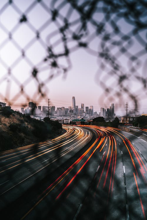 Free Time Lapse Photography of City Through Chain fence Stock Photo