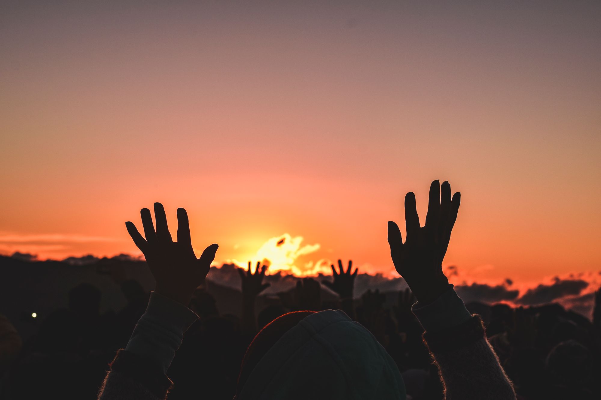 Congregation in silhouette with hands raised at sunset