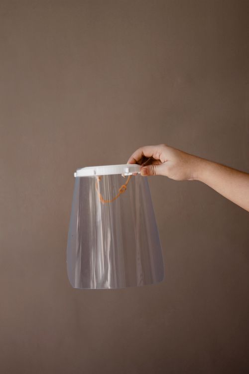 Free A hand holding a clear protective face shield against a neutral background. Stock Photo