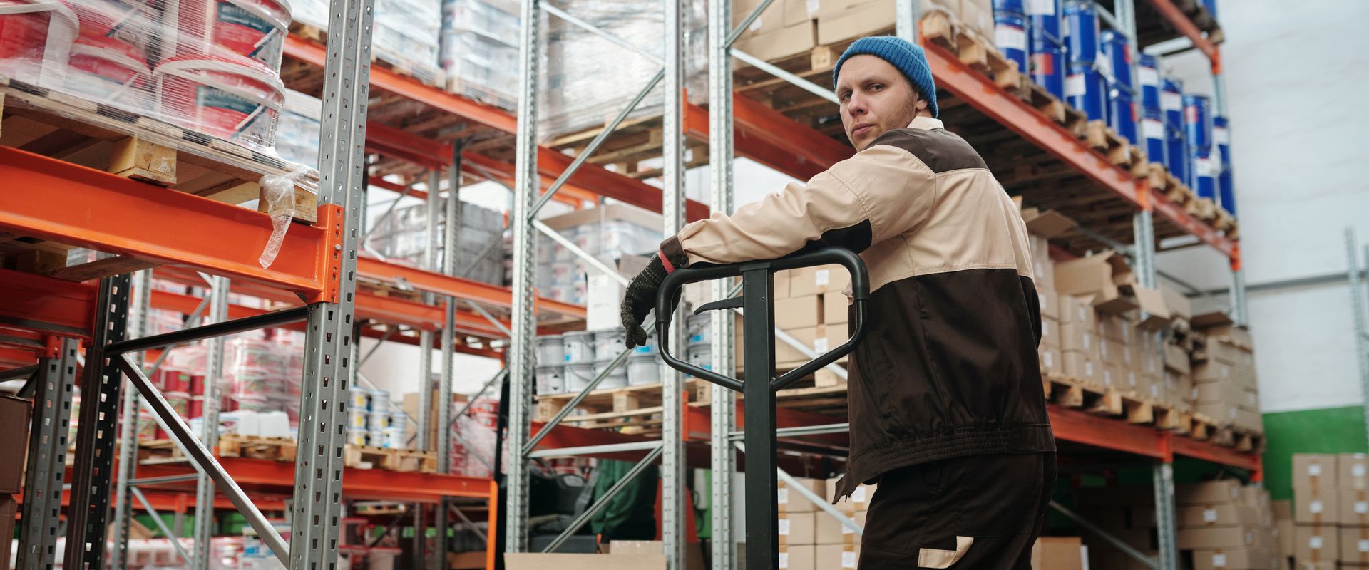Warehouse worker moving stacked boxes of products with a pallet jack