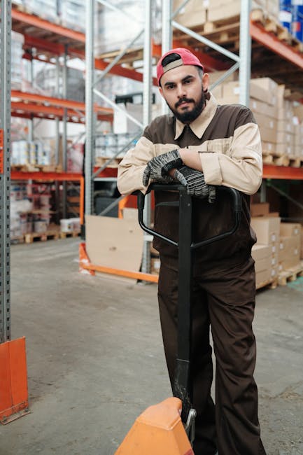 Portrait of a warehouse worker resting on a pallet jack in an industrial storage environment.