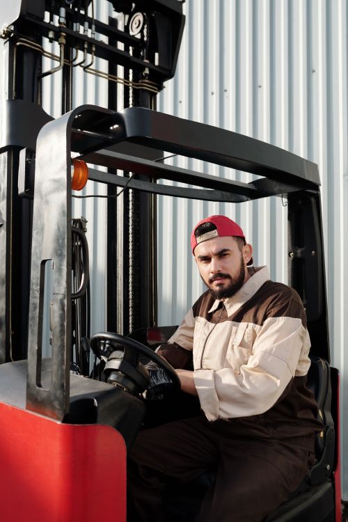 Free Portrait of a forklift operator inside a warehouse, wearing a uniform and cap. Stock Photo