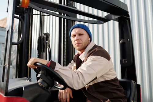 Free Male forklift operator wearing a blue beanie and work uniform, sitting outside on a sunny day. Stock Photo