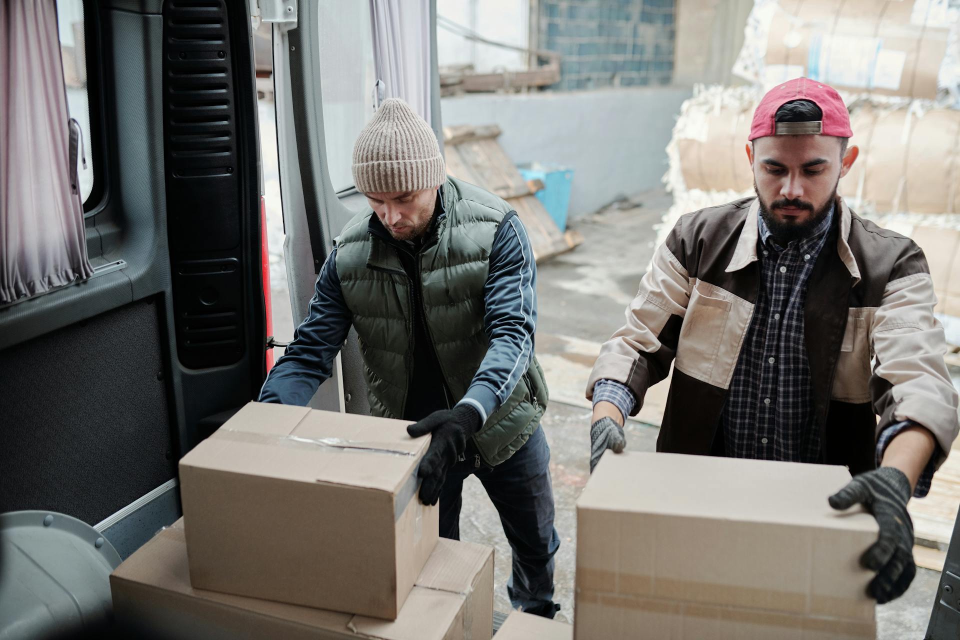 Two male workers loading packages into a delivery van, teamwork in logistics.