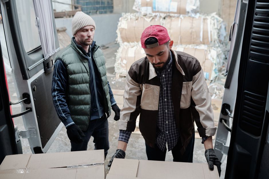 Two men loading cardboard boxes into a delivery van at an urban site. Two men loading cardboard boxes into a delivery van at an urban site.