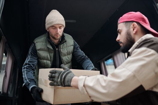Two men unloading a cardboard box from a delivery van, showcasing teamwork.
