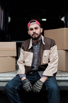 Bearded man sitting in a van surrounded by boxes, portraying a delivery worker on the job.