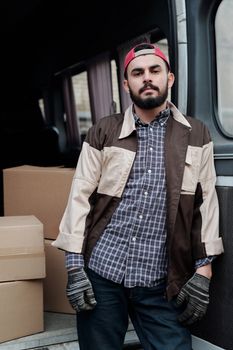 Delivery man in casual clothing standing by boxes in a van, showcasing logistics and transportation services.
