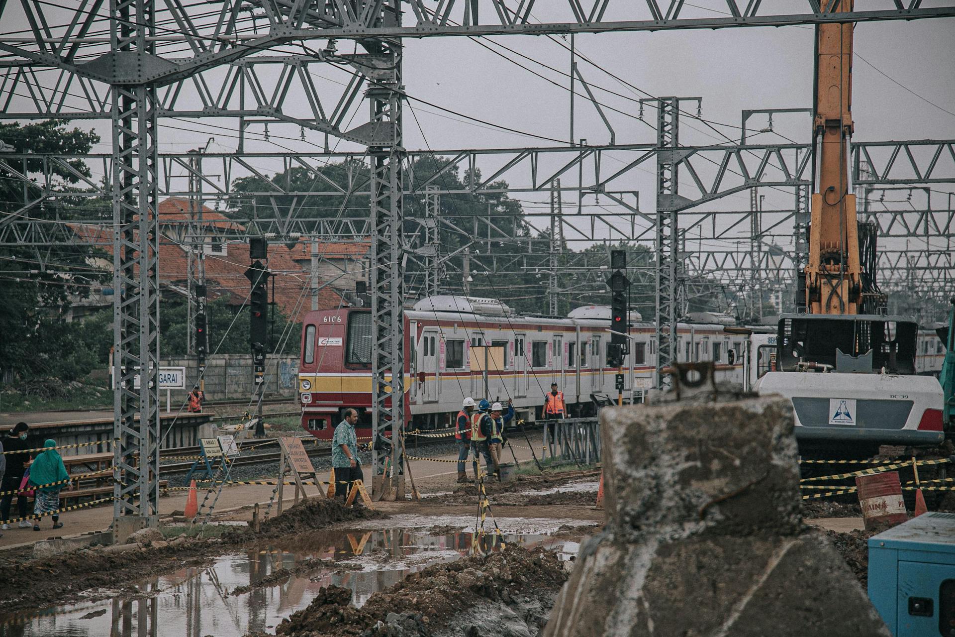 A bustling railway construction site with trains, workers, and heavy machinery on a muddy platform.