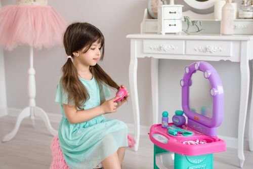 Free Young girl in green dress playing with pretend vanity toys, sitting indoors. Stock Photo
