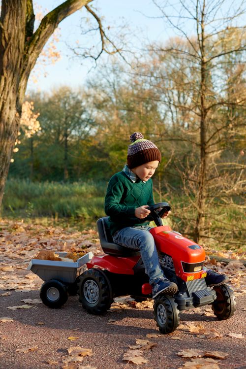 Free Boy playing on a toy tractor in a park during fall, surrounded by fallen leaves. Stock Photo