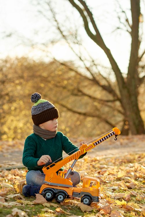 Free A young boy enjoys playing with a crane truck surrounded by autumn leaves outdoors. Stock Photo