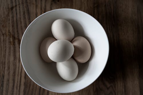 Top view of pile of white cooked chicken eggs in ceramic bowl on wooden table at home
