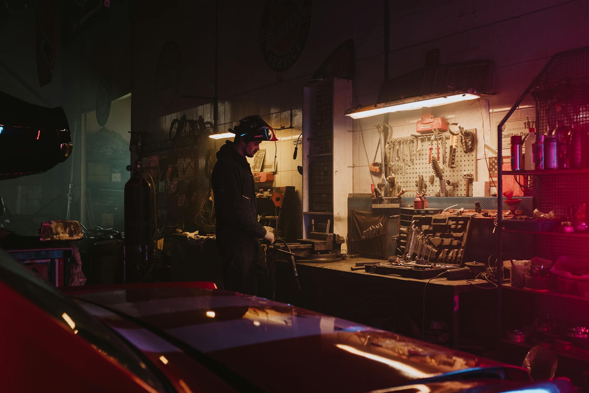 Mechanic working in a dimly lit garage workshop surrounded by tools and equipment.