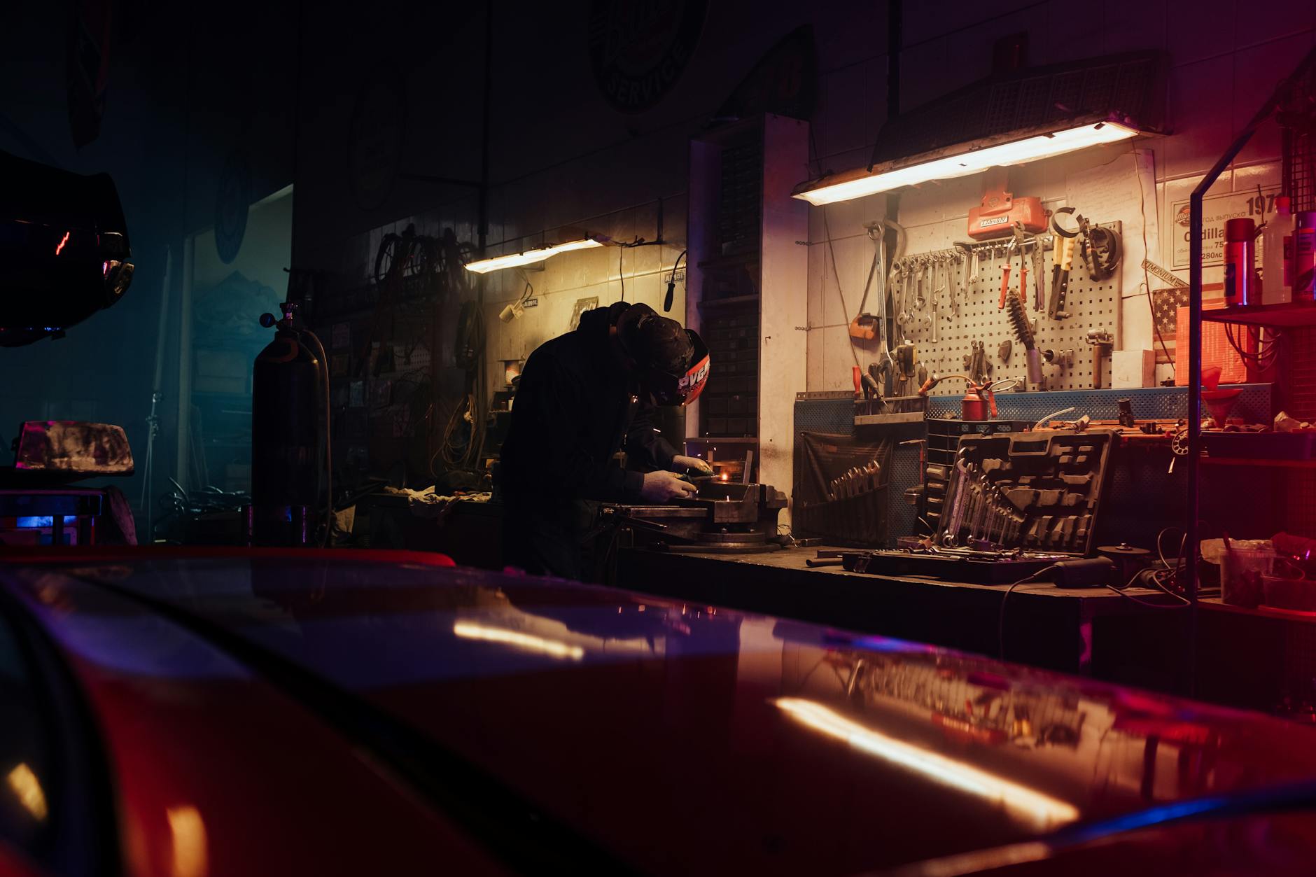 A mechanic diligently working on a car part in a tool-filled garage.